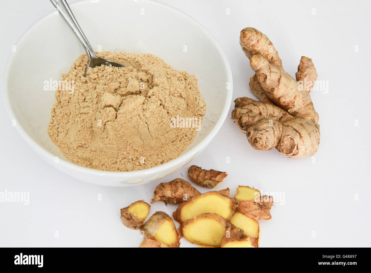 Gingembre en poudre dans un bol avec cuillère en métal, racine de gingembre, et des morceaux de racine de gingembre isolated on white Banque D'Images