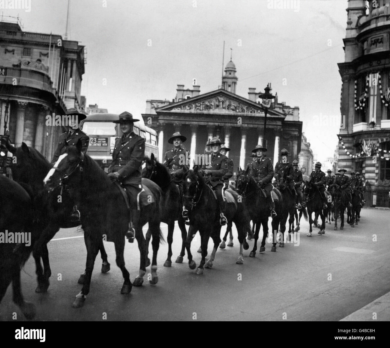 Les membres de la Gendarmerie royale du Canada, passent leurs chevaux à travers la ville de Londres, après la Bourse royale et la Banque d'Angleterre, à gauche, en route du Royal Albert Dock vers les lignes de chevaux à Hyde Park. Les quarante-six chevaux doivent être criés dans la procession du Couronnement. Banque D'Images