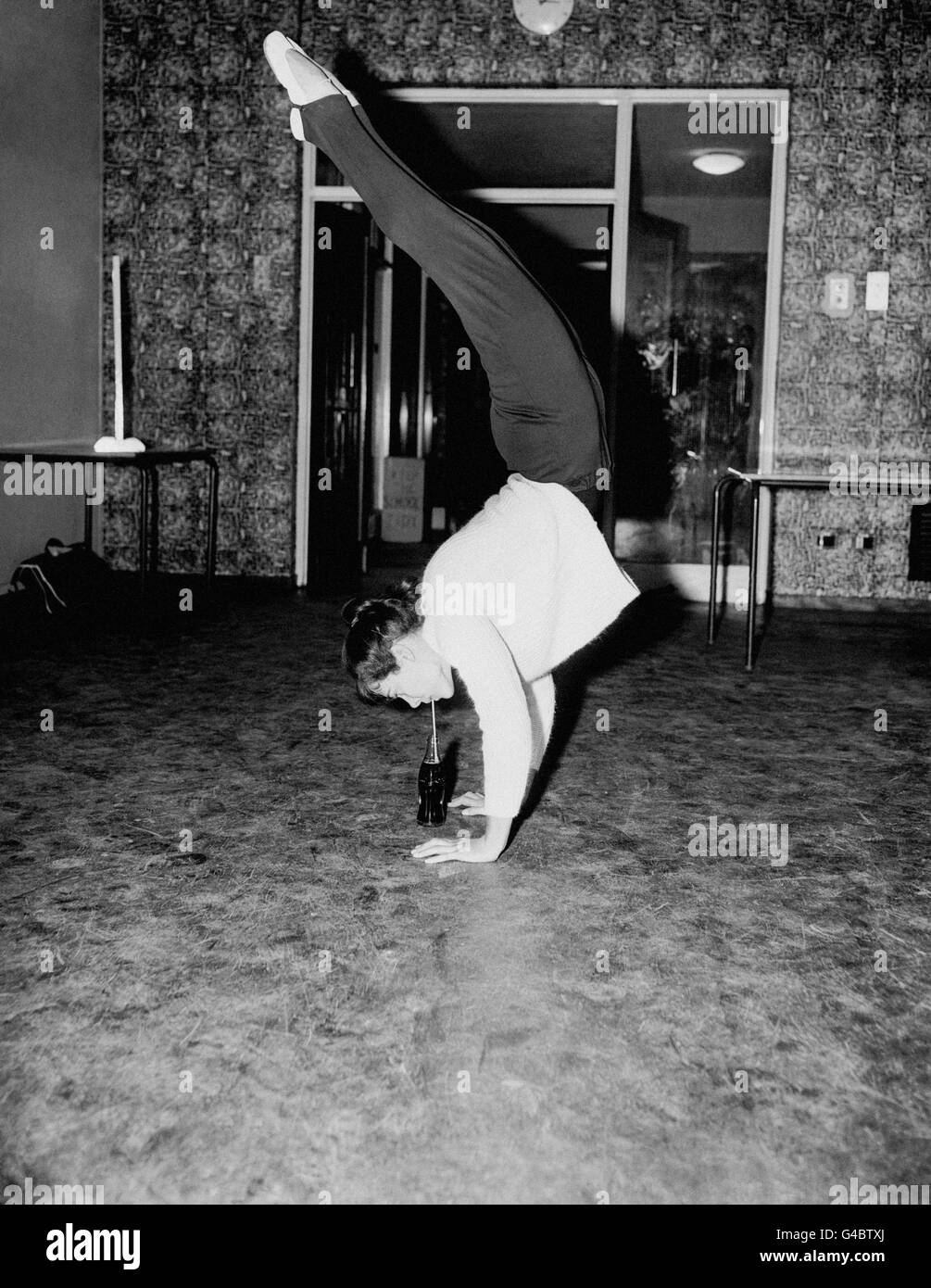 Après avoir fait une démonstration, Monica Rutherford, âgée de 17 ans, championne de gymnastique féminine, trouve une position peu orthodoxe pour siroter une boisson rafraîchissante. Banque D'Images