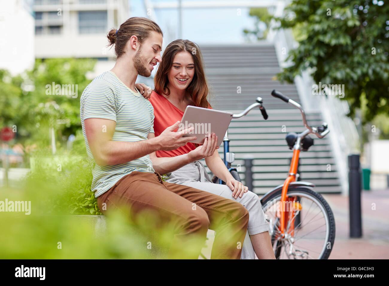 Parution du modèle. Young couple sitting on wall with digital tablet. Banque D'Images