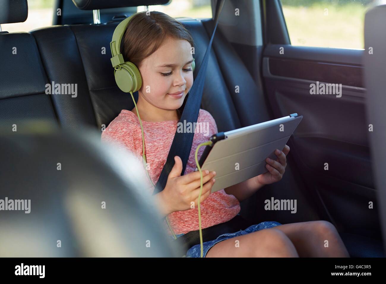 Parution du modèle. Fille dans le siège arrière de la voiture portant des écouteurs, regarder un film. Banque D'Images