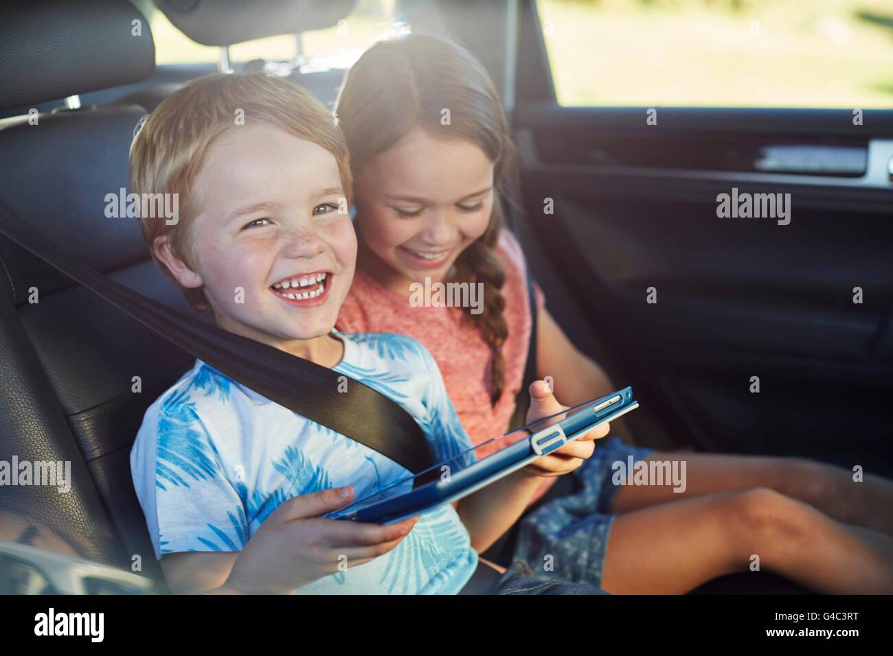 Parution du modèle. Frère et soeur dans le siège arrière de la voiture-port de la ceinture de sécurité, à l'aide d'une tablette numérique. Banque D'Images