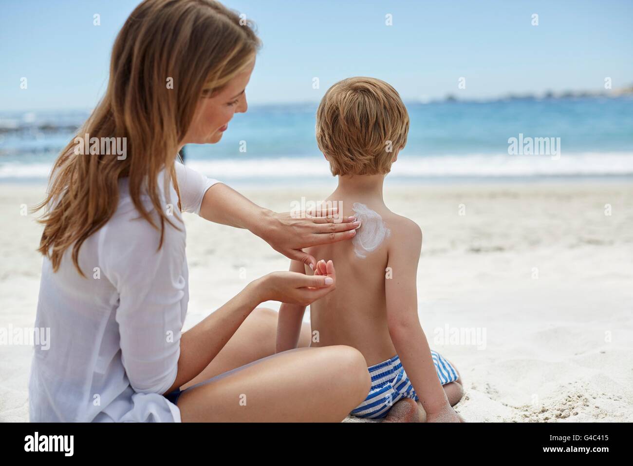 Parution du modèle. Mère l'application de la crème solaire à son fils sur la plage. Banque D'Images