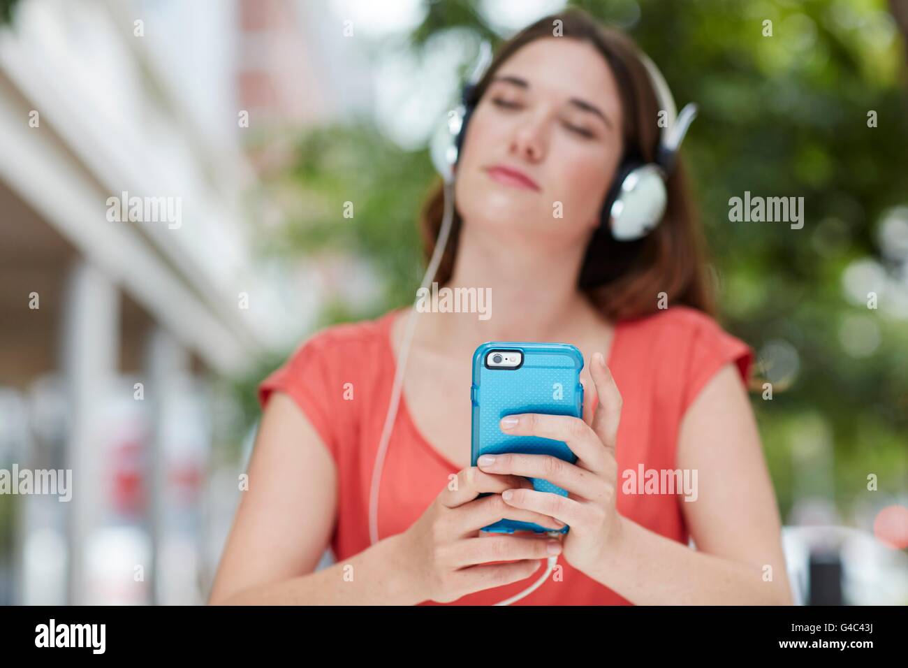 Parution du modèle. Young woman wearing headphones listening to music sur smartphone. Banque D'Images