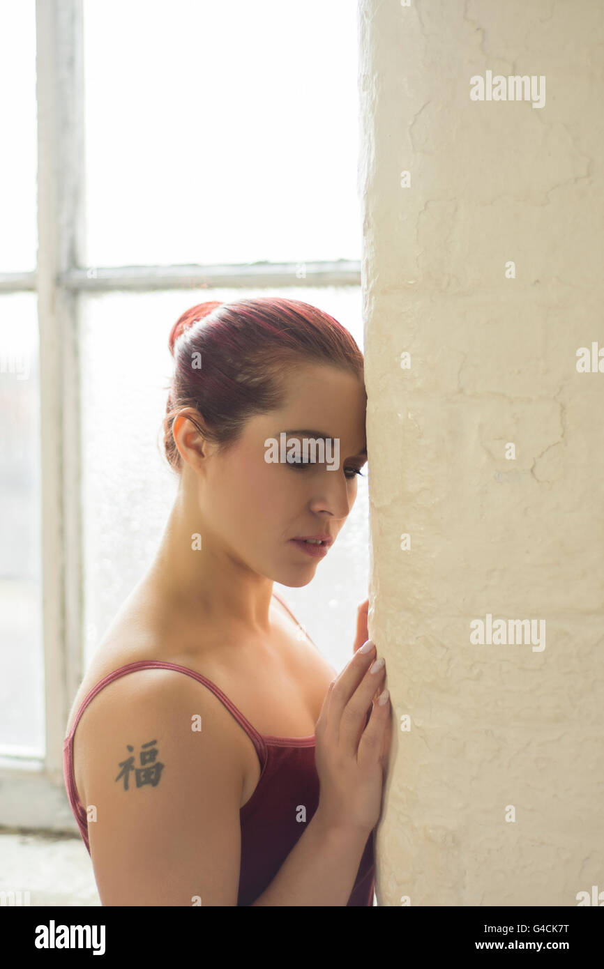 Femme tatouée appuyé contre le mur par la fenêtre Banque D'Images