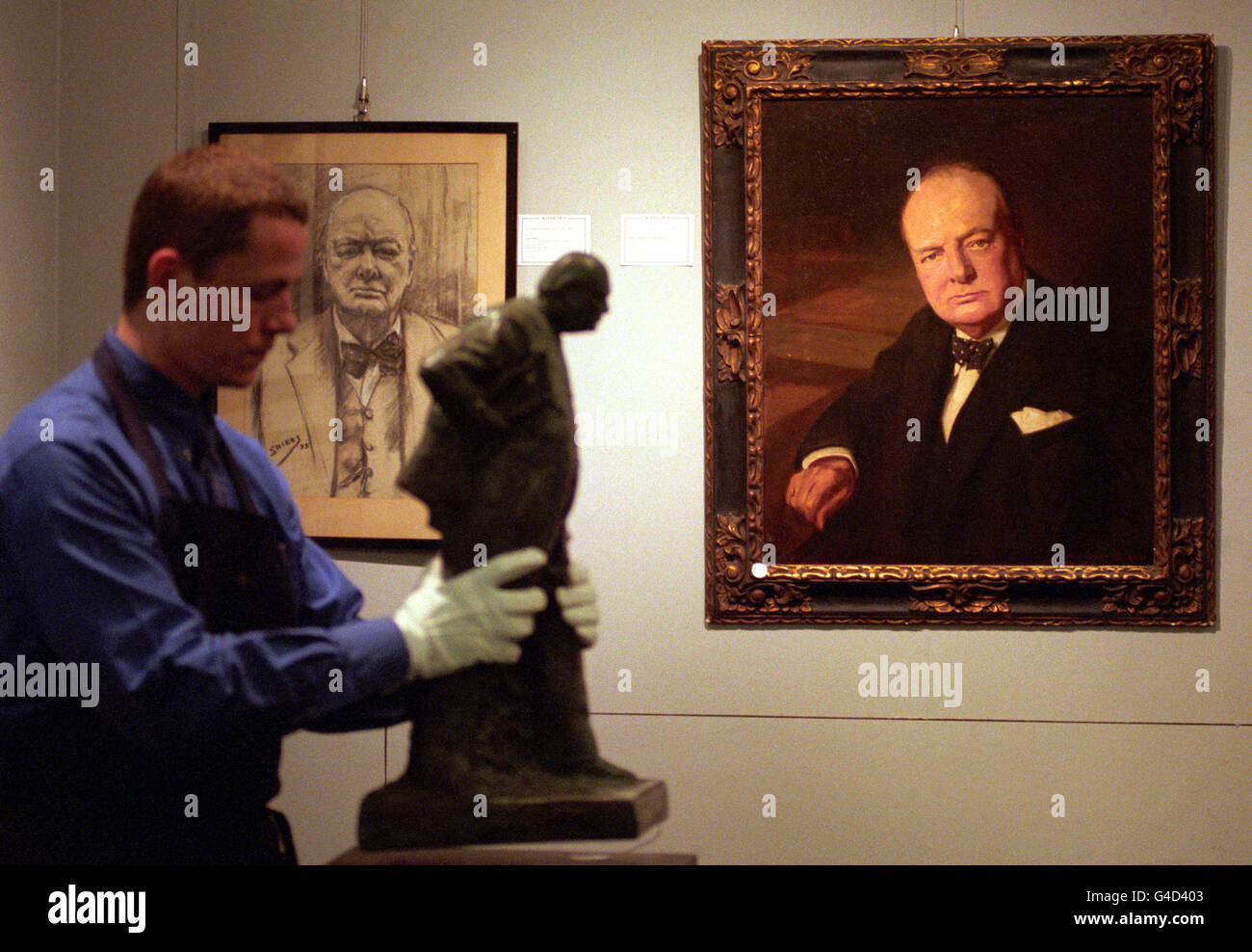 Un homme de Sotheby's déplace une statue d'Oscar Nemon de Sir Winston Churchill devant un portrait de John Berrie avant la vente de souvenirs politiques. Banque D'Images