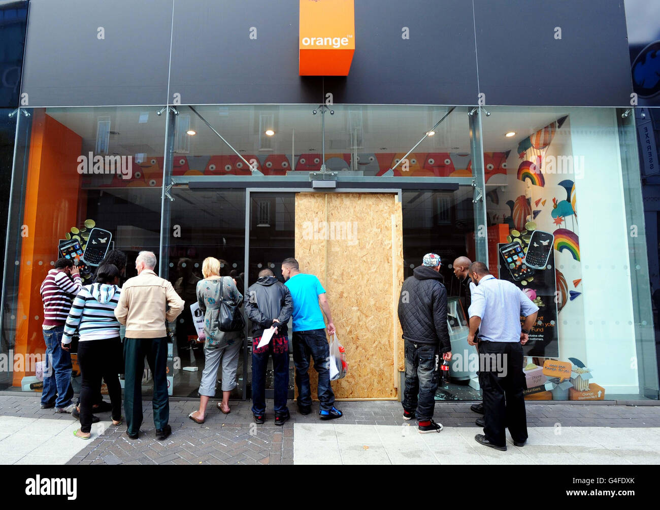 Les gens regardent l'intérieur d'un magasin Orange près du centre commercial Bullring de Birmingham après avoir été pillé la nuit dernière. Banque D'Images