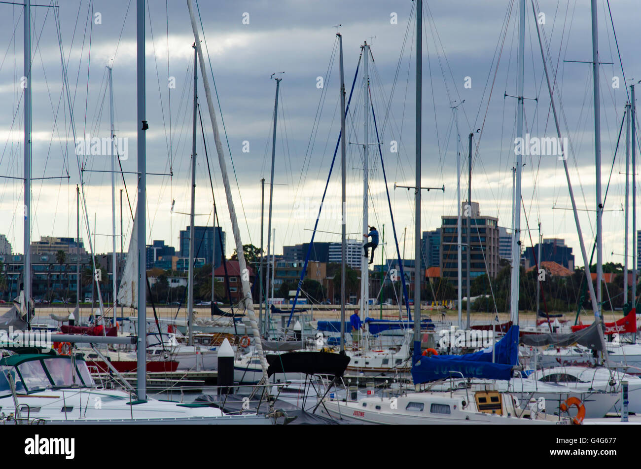 Un homme escalade un mât de yacht dans une marina à St Kilda à Melbourne, en Australie, par une journée nuageux et couvert Banque D'Images