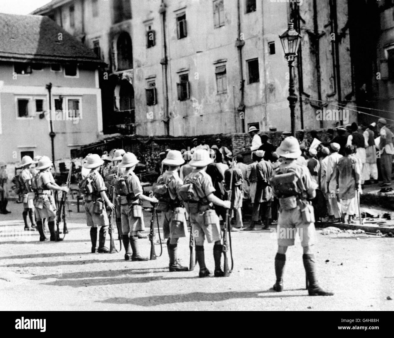 Des policiers britanniques et indiens ont fait le bilan des émeutiers de Patan à Dongri, Bombay, tandis que les soldats britanniques regardent, lors des émeutes hindoues et musulmanes de 1932. Banque D'Images