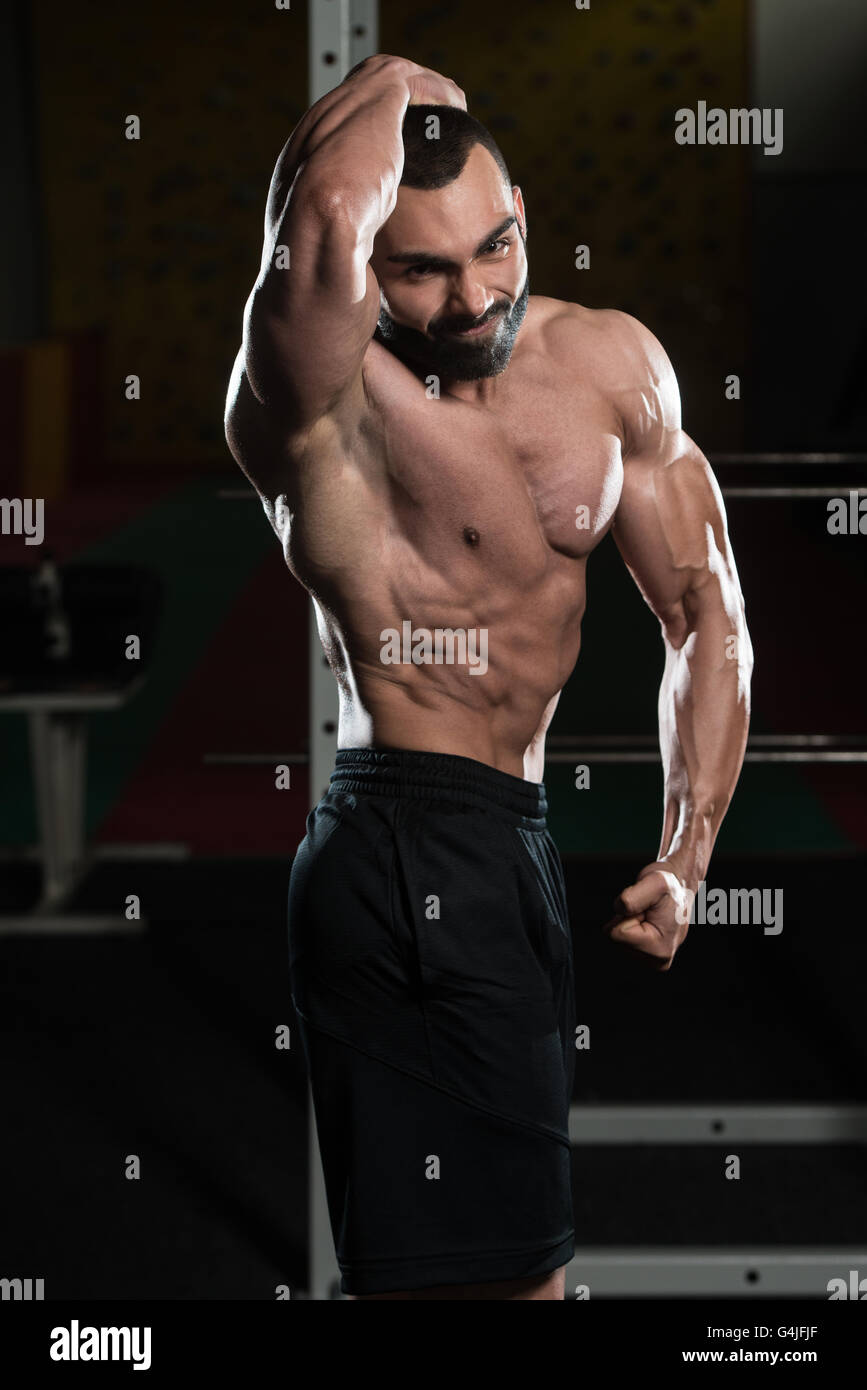 Jeune homme debout forte dans la salle de sport et Flexing Muscles - Remise en forme musculaire Bodybuilder Athletic Model Posing montrant après Abs Banque D'Images