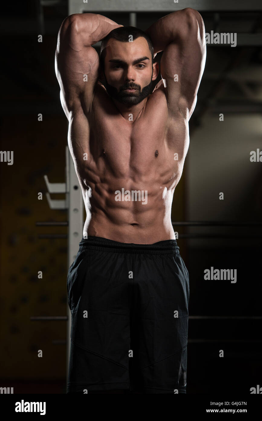 Jeune homme debout forte dans la salle de sport et Flexing Muscles - Remise en forme musculaire Bodybuilder Athletic Model Posing montrant après Abs Banque D'Images