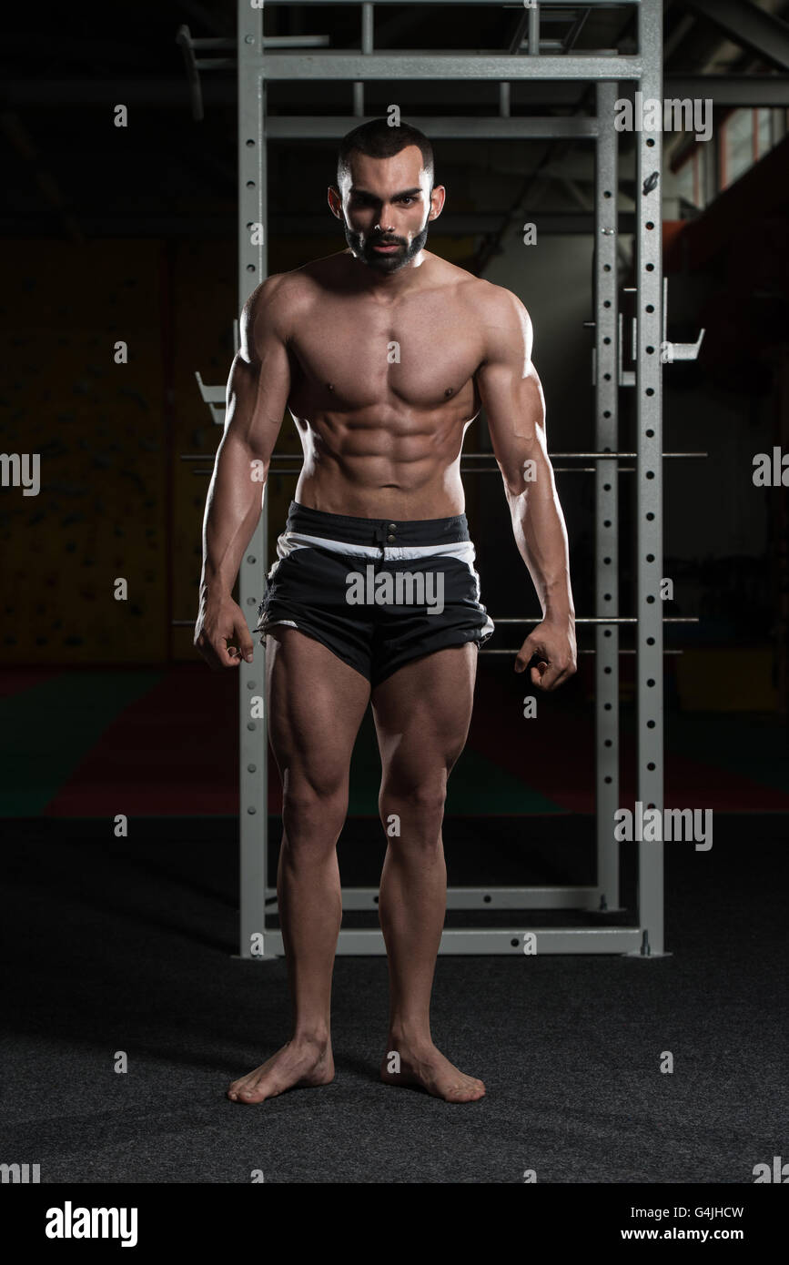 Jeune homme debout forte dans la salle de sport et Flexing Muscles musculaire - Fitness Model Posing Bodybuilder athlétiques exercices après Banque D'Images