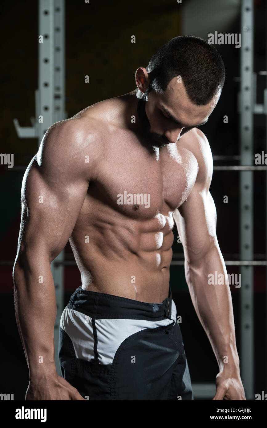 Jeune homme debout forte dans la salle de sport et Flexing Muscles musculaire - Fitness Model Posing Bodybuilder athlétiques exercices après Banque D'Images