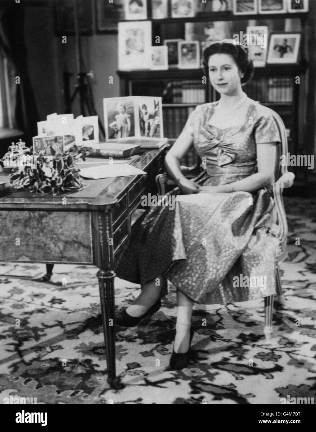 La Reine, dans une robe de couleur or, est vue dans la long Library de Sandringham peu après avoir fait la traditionnelle émission du jour de Noël à ses peuples. Sur le bureau se trouvent des portraits du prince Charles et de la princesse Anne. L'émission a été télédiffusée pour la première fois par ce yer et a été diffusée par la BBC et ITV. C'était le 25e anniversaire du premier message radio adressé au Commonwealth par son grand-père, le roi George V. Banque D'Images