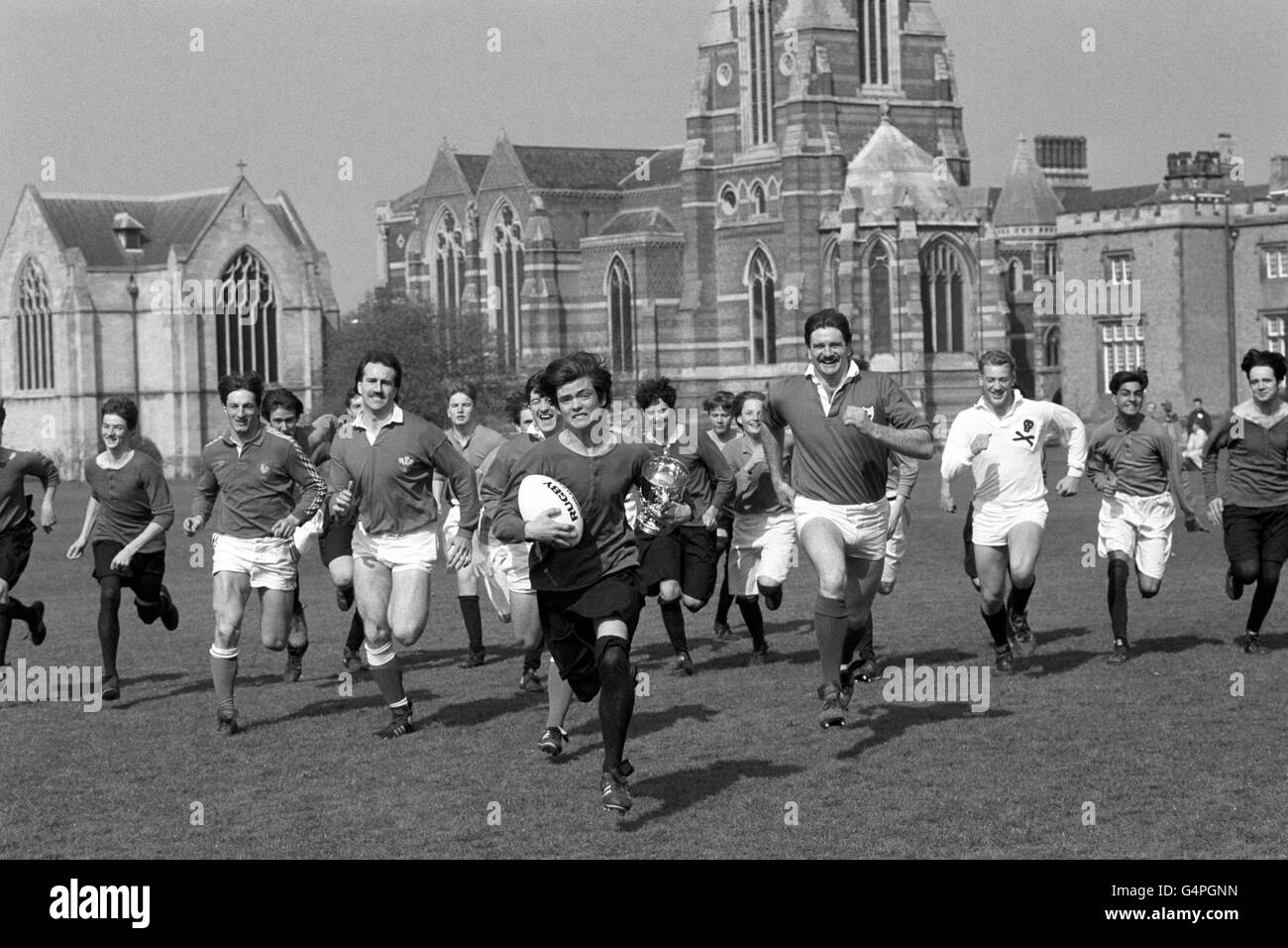 Daniel Enright-Mooney, étudiant à l'école de rugby, en tant que William Webb Ellis, réenforme la scène en 1823 lorsque le match de rugby est né à l'école de Warwickshire. Il est chassé par des étoiles, de gauche à droite, Philippe Sella de France, Bob Norster du pays de Galles, Robert Jones du pays de Galles, et Willie Anderson d'Irlande, et le reste de l'équipe scolaire. Banque D'Images