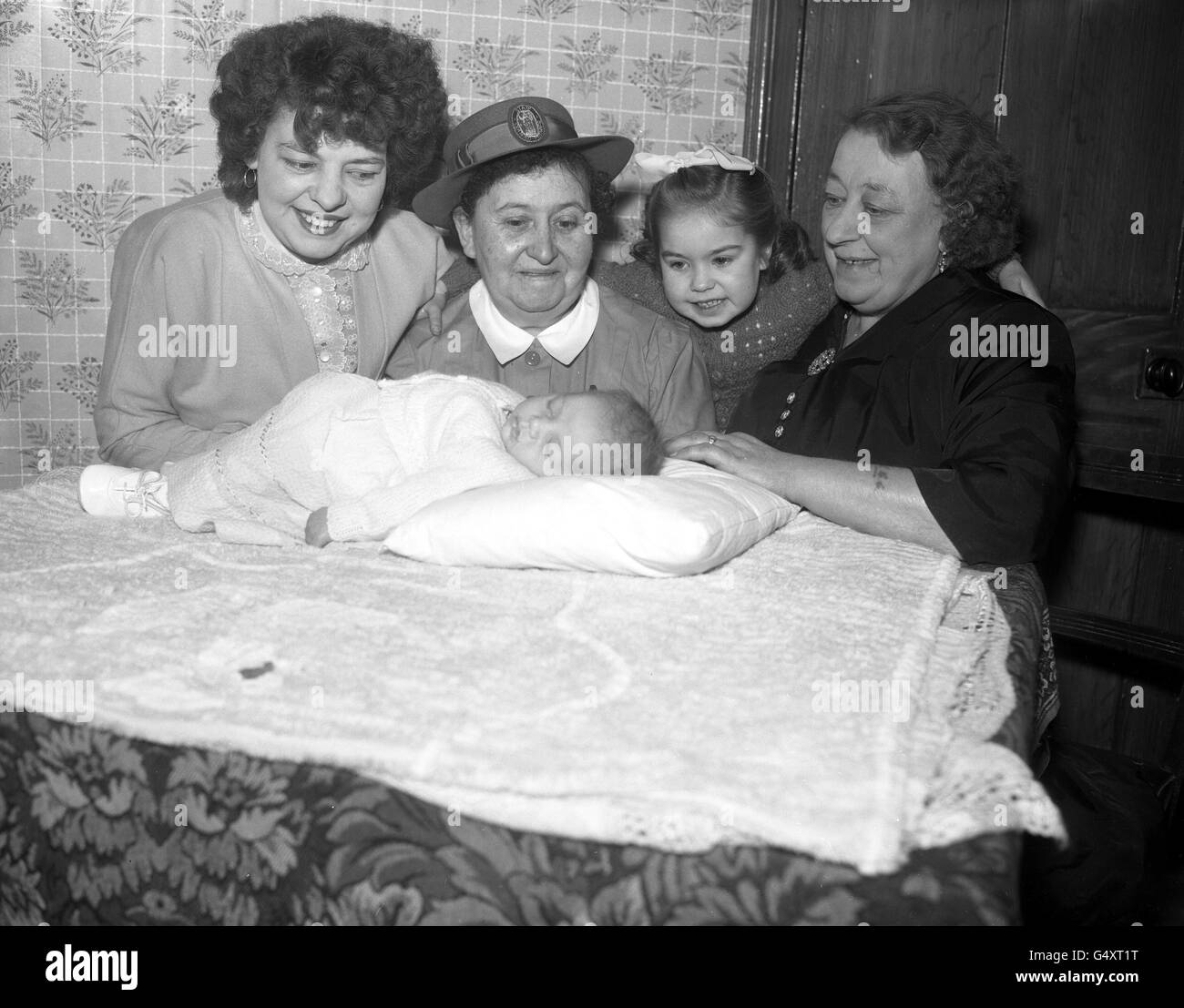 Mlle Elsie A Walkerdine, qui prend sa retraite après 40 ans comme sage-femme domiciliaire, rend visite à une famille à Deptford, Londres, pour voir le bébé Colin, dont elle a assisté à la naissance le 26 novembre 1957. Mlle Walkerdine a également aidé à livrer la sœur Barbara Ann, âgée de six ans, de Colin, et sa mère, Mme Joyce Leary, âgée de 30 ans, qui sont photographiées ici avec la grand-mère Mme North. Mlle Walkerdine, qui vit à Deptford et est bien connue dans le district, a livré près de 4,000 bébés. Banque D'Images