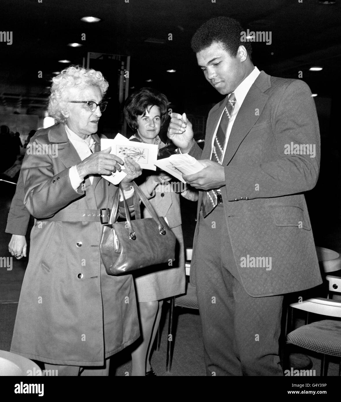 Le boxeur américain Muhammad Ali donne des autographes aux fans féminins de l'aéroport d'Heathrow, avant de prendre l'avion pour l'Arabie Saoudite, pour un pèlerinage musulman à la Mecque où il prévoit de célébrer Omra. Banque D'Images