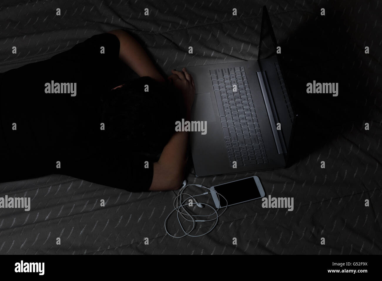 Teen girl s'endort avec son ordinateur toujours allumé tandis que dans le lit. Effet de lumière sur le clavier de l'ordinateur. Banque D'Images