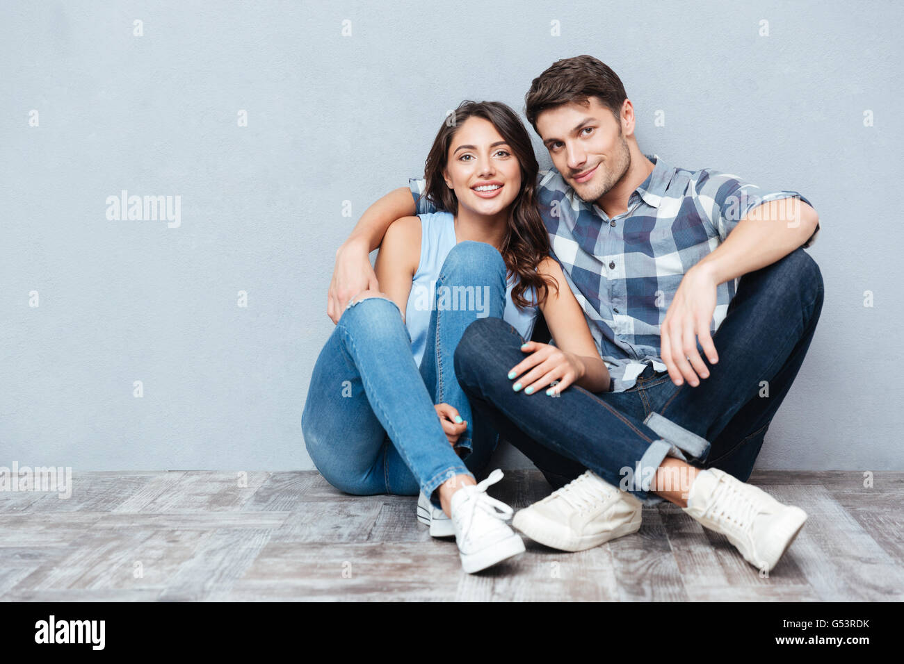 Jeune couple assis sur le sol dans leur appartement isolé sur fond gris Banque D'Images