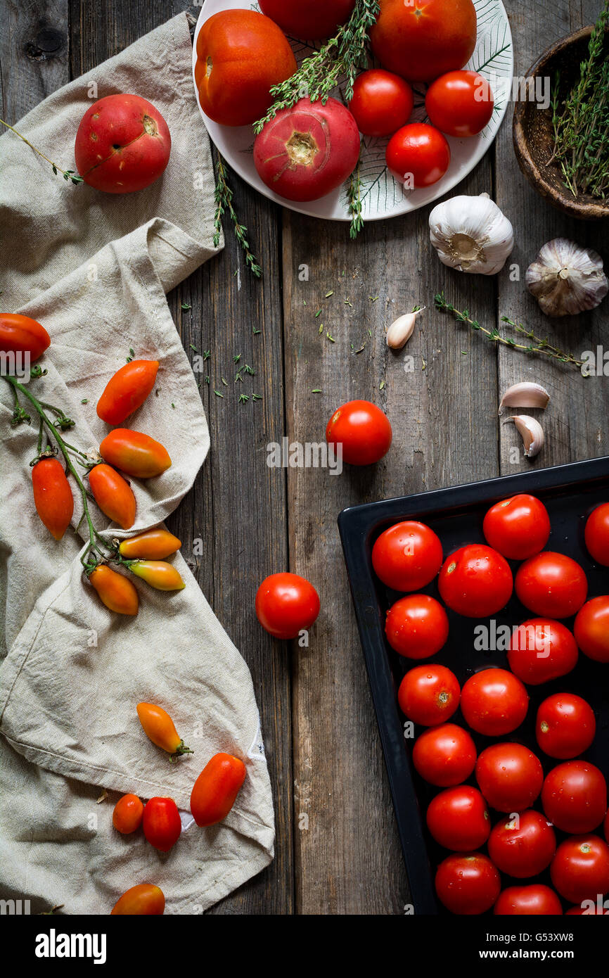 La vie encore de tomates. Heirloom frais tomates cerises, les tomates biologiques, l'ail et le thym sur fond de bois rustique Banque D'Images