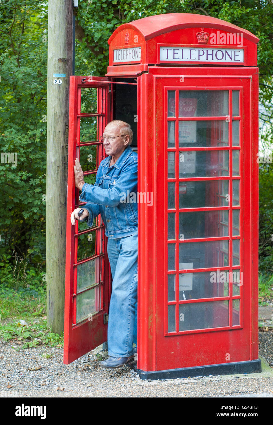 L'homme en sortant d'un ancien style British red téléphone fort dans Amberley, West Sussex, Littlehampton, Angleterre, Royaume-Uni. Banque D'Images