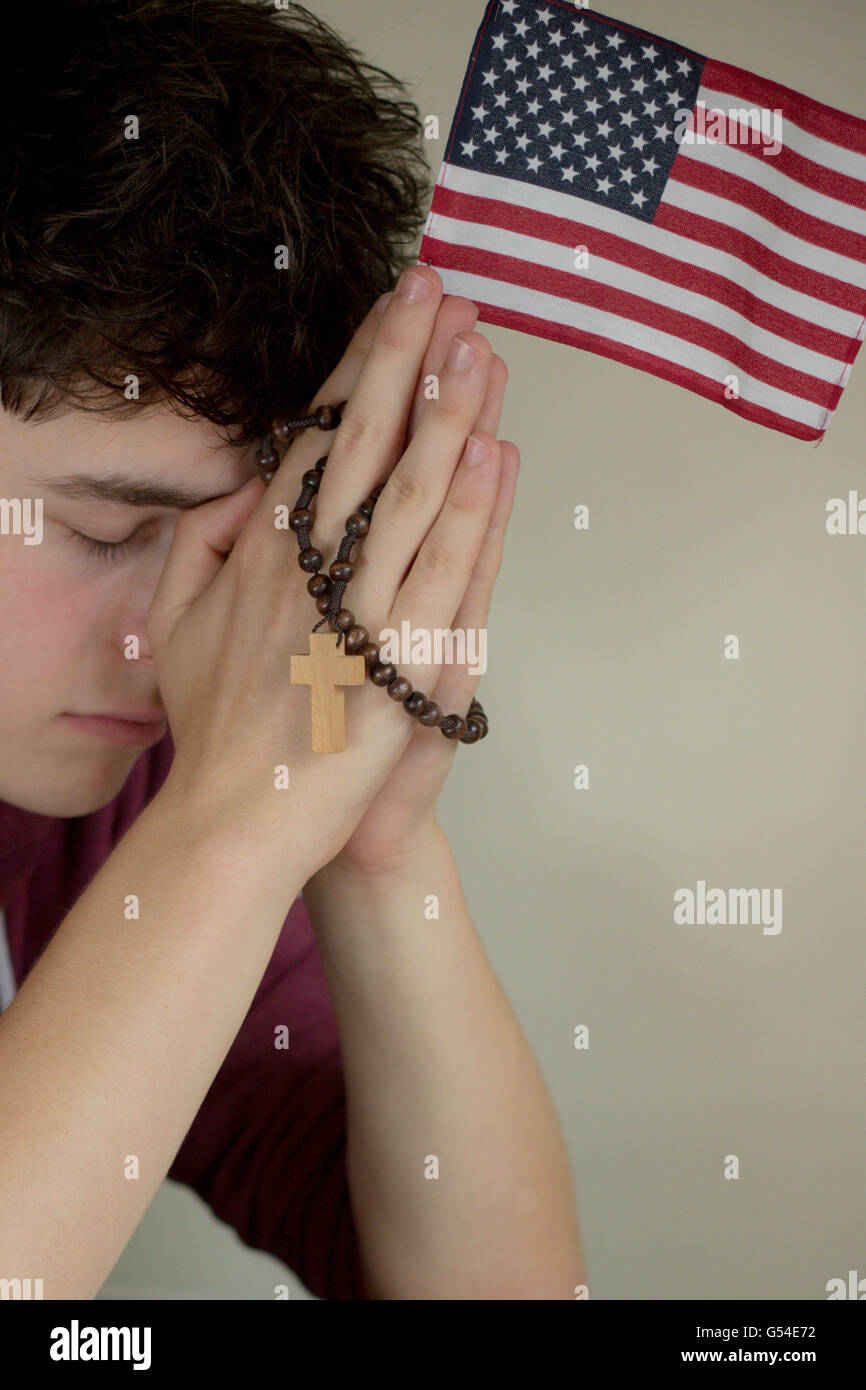 Teenage boy prier avec un chapelet et drapeau Américain Banque D'Images
