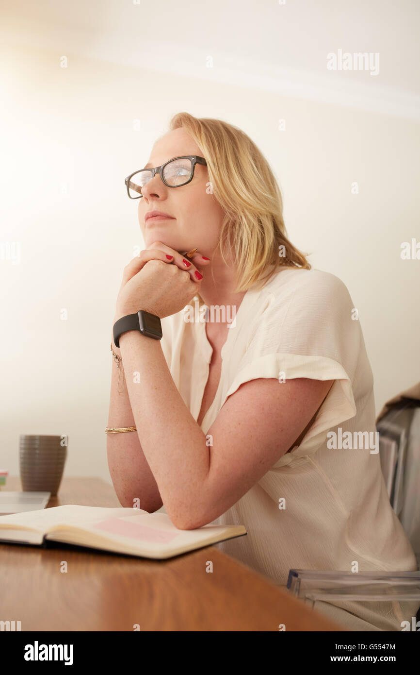 Portrait of mature businesswoman assise à son bureau et à l'écart de pensée. Portrait femme assise dans son bureau à domicile avec Banque D'Images