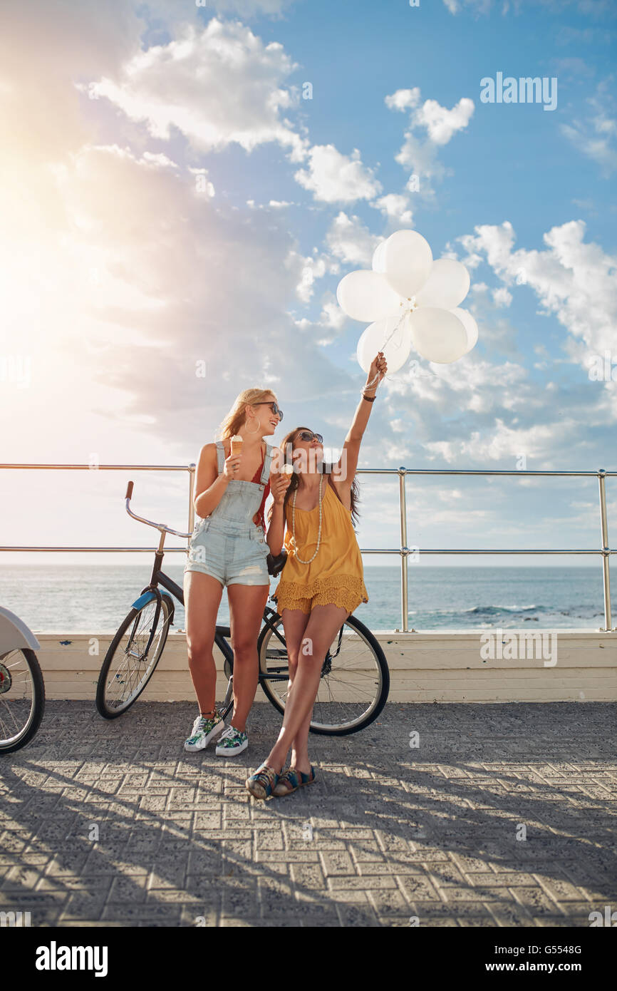 Tourné en plein air de deux femmes se tenant ensemble avec des vélos et des ballons sur route côtière. Les meilleurs amis s'amuser sur leurs vacatio Banque D'Images