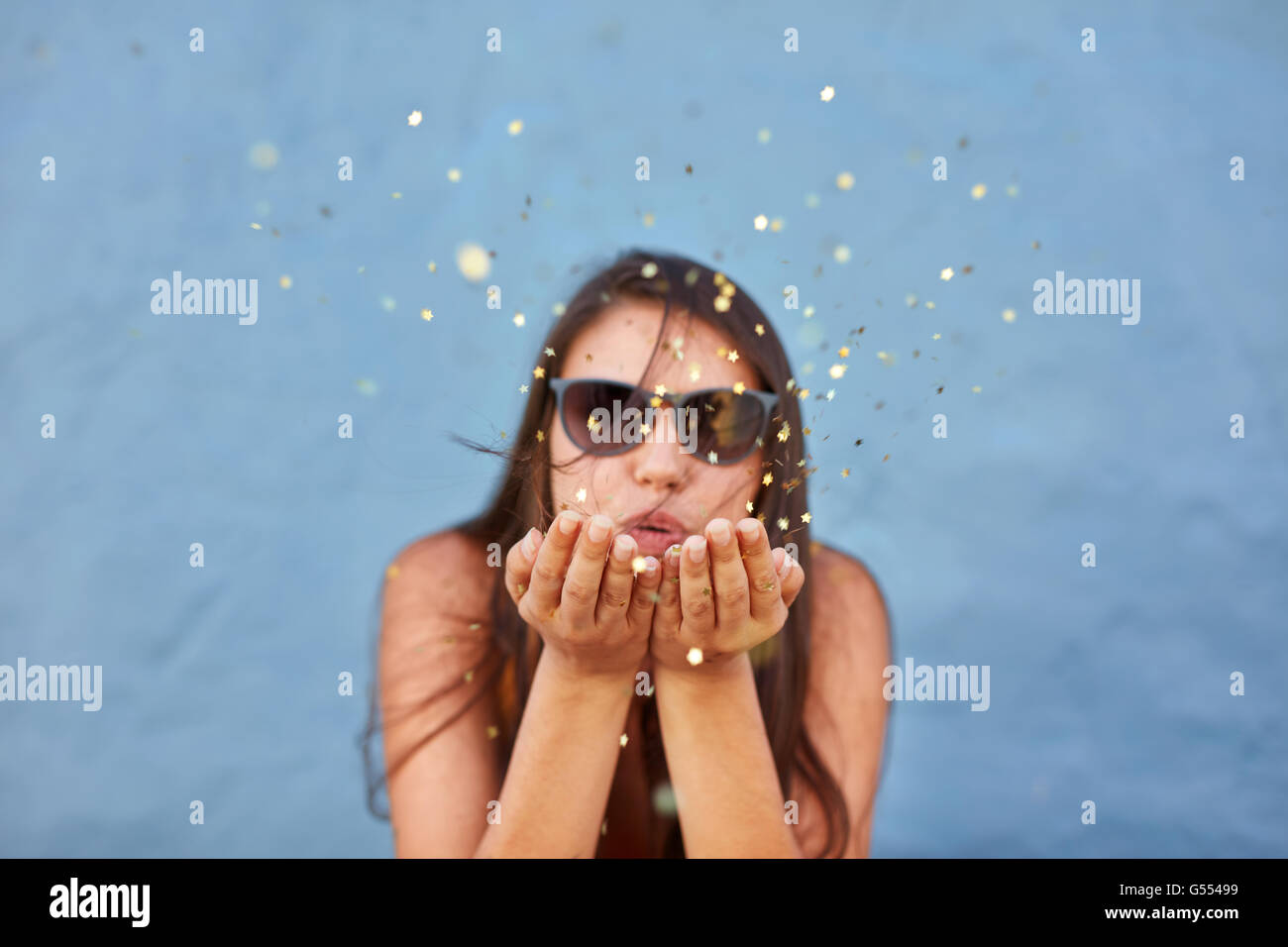 Portrait de belle jeune femme soufflant une rafale de magic glitter sur fond bleu Banque D'Images