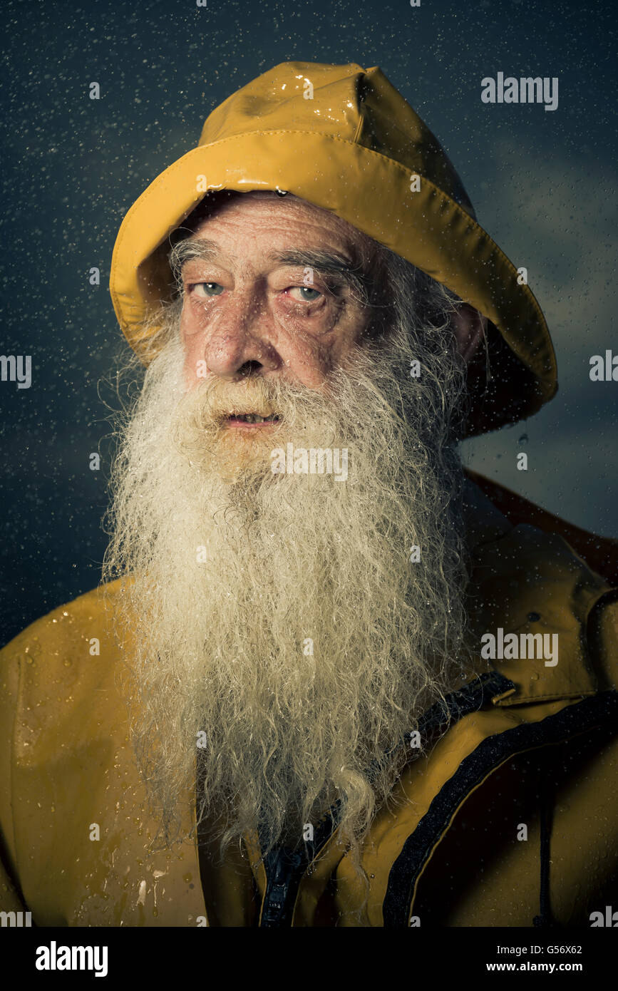 Homme barbu dans un fisherman's sou'wester manteau jaune et chapeau dans la pluie. Banque D'Images