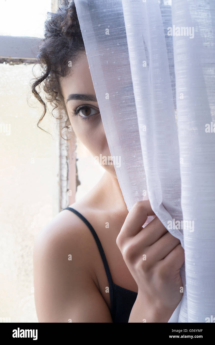 Femme de se cacher derrière les blinds Banque D'Images