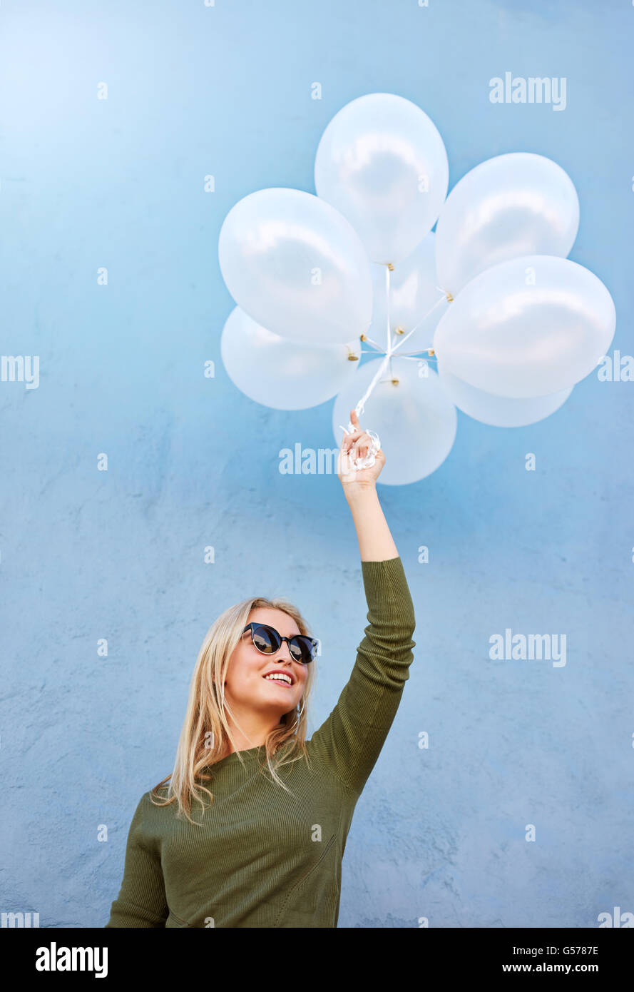 Coup de jeune joyeuse modèle féminin avec des ballons. Caucasian woman in sunglasses contre fond bleu. Banque D'Images