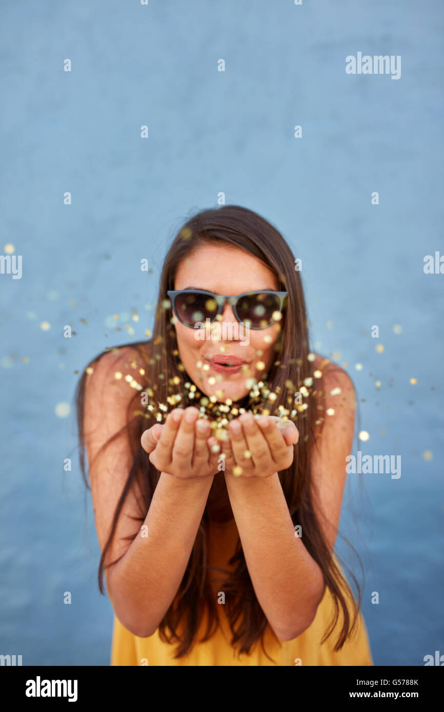 Portrait of happy young female model blowing confetti dans l'air au-dessus de l'arrière-plan lumineux Banque D'Images