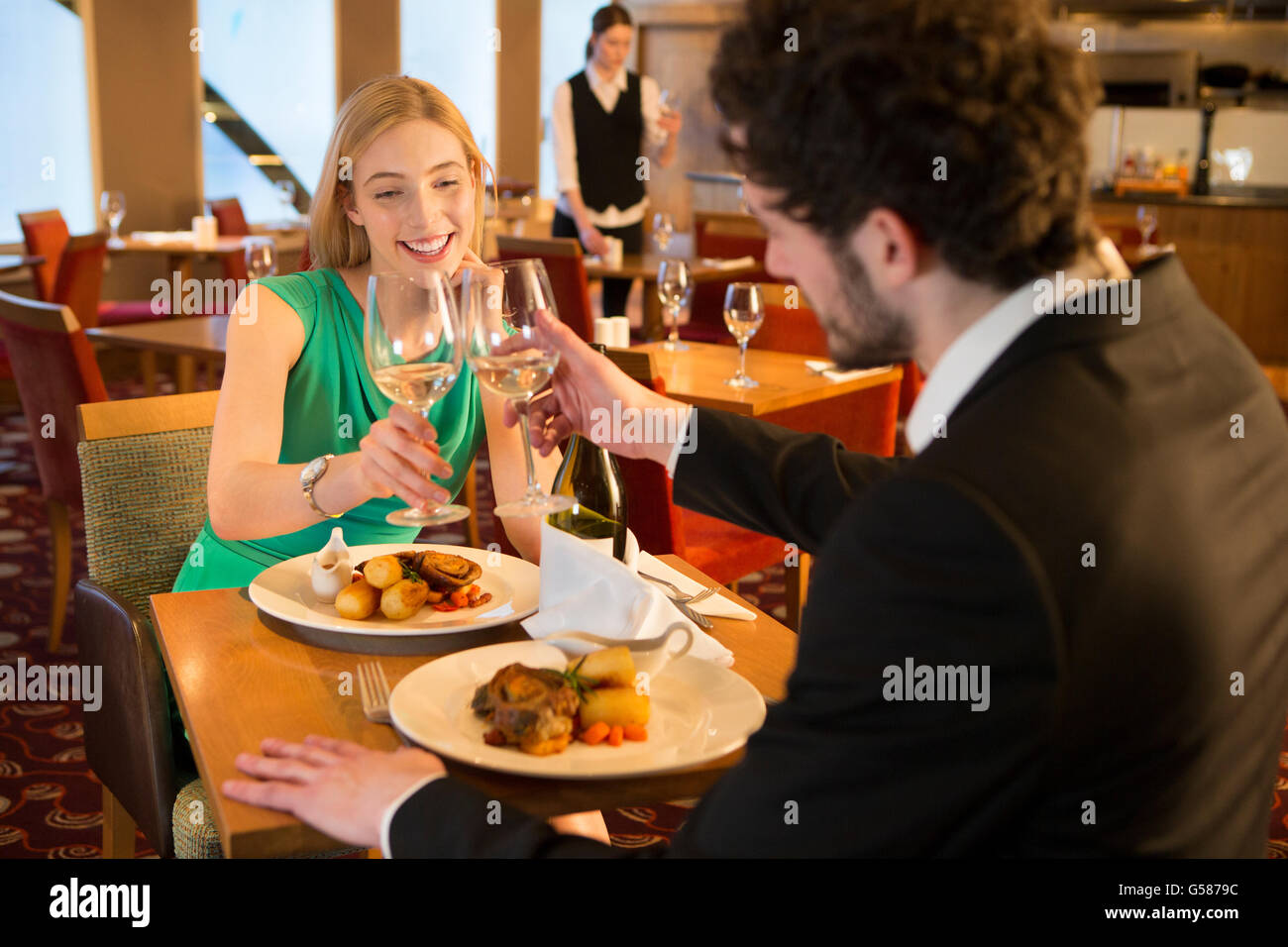 Jeune couple toasting leurs verres de champagne autour d'un repas dans un restaurant. Banque D'Images