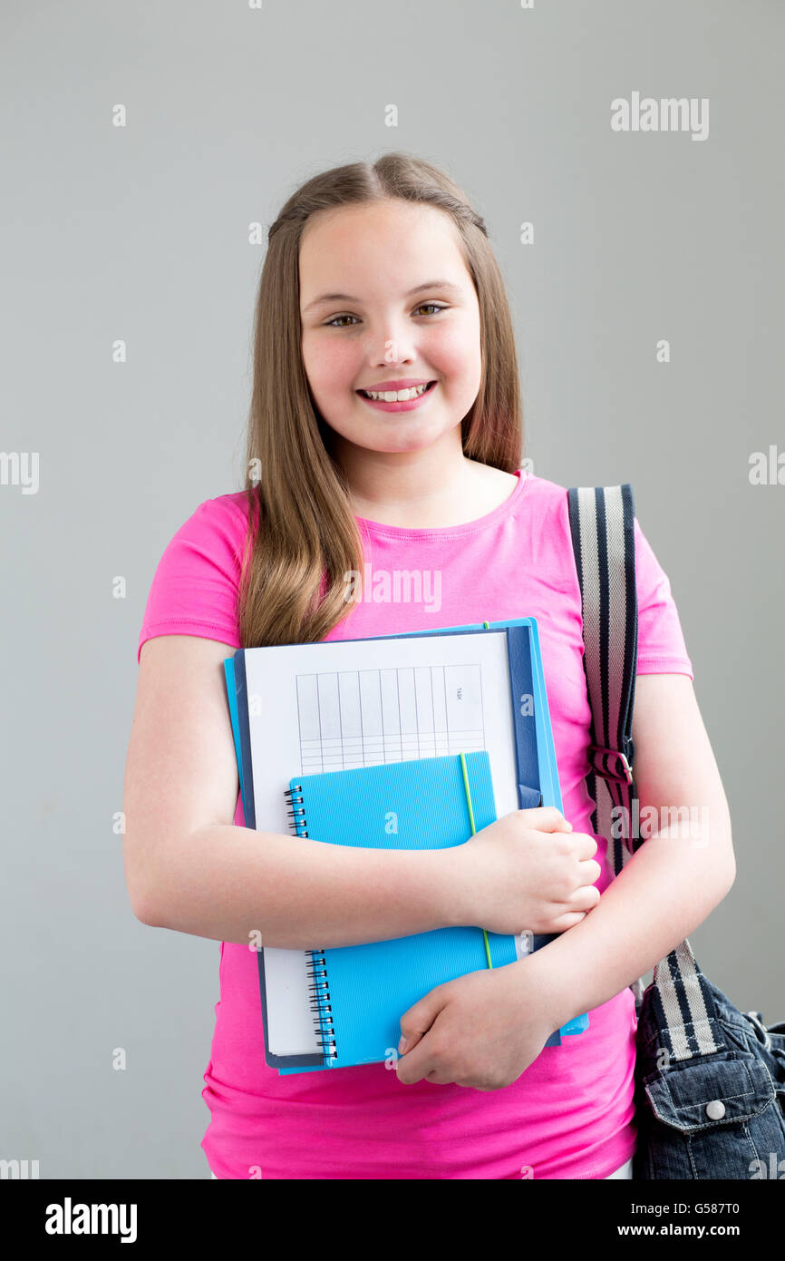 Jeune écolière sourire pour la caméra avec des dossiers dans la main et un sac sur son épaule. Elle se tient contre un dos uni Banque D'Images
