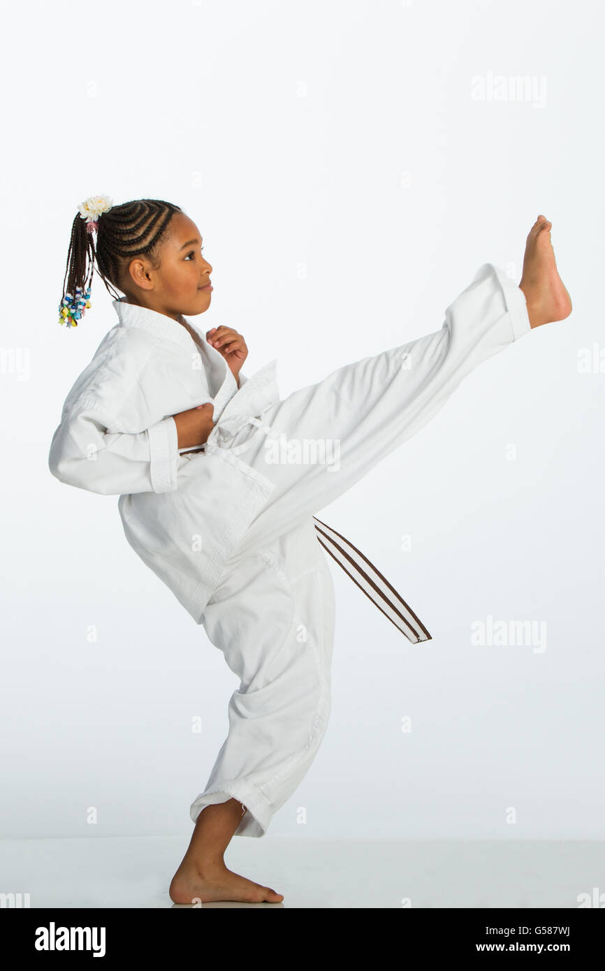 Young mixed race girl posing dans un coup de karaté. Elle porte un carategi et est debout sur un fond blanc. Banque D'Images