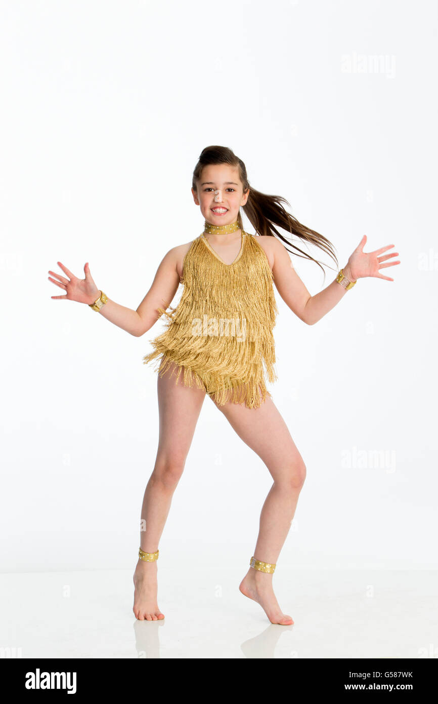 Jeune danseuse en costume d'or. Elle danse sur un fond blanc et souriant à la caméra. Banque D'Images