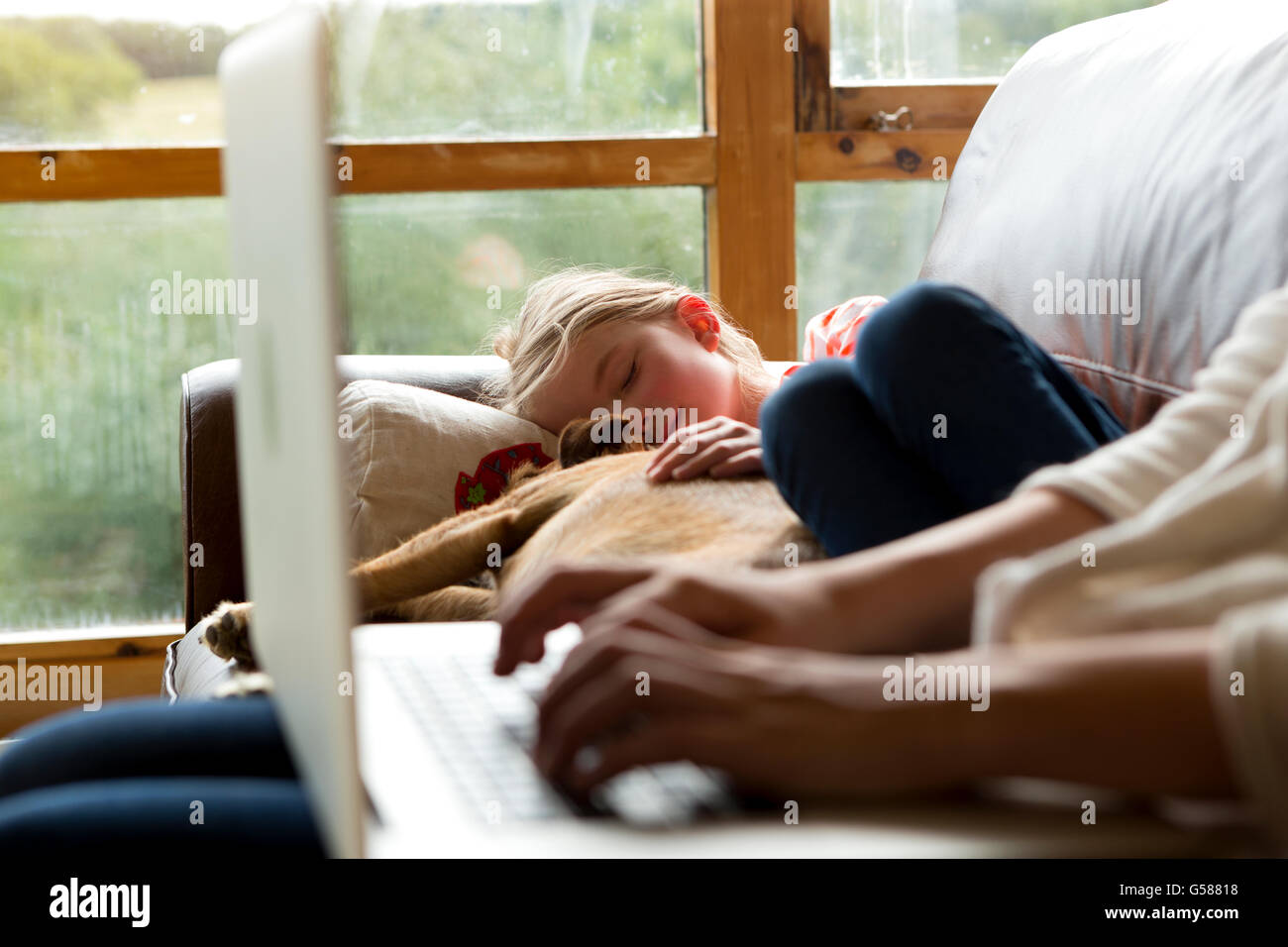 Femme à l'aide d'un ordinateur portable avec sa fille et son chien dormir ensemble à côté d'elle Banque D'Images