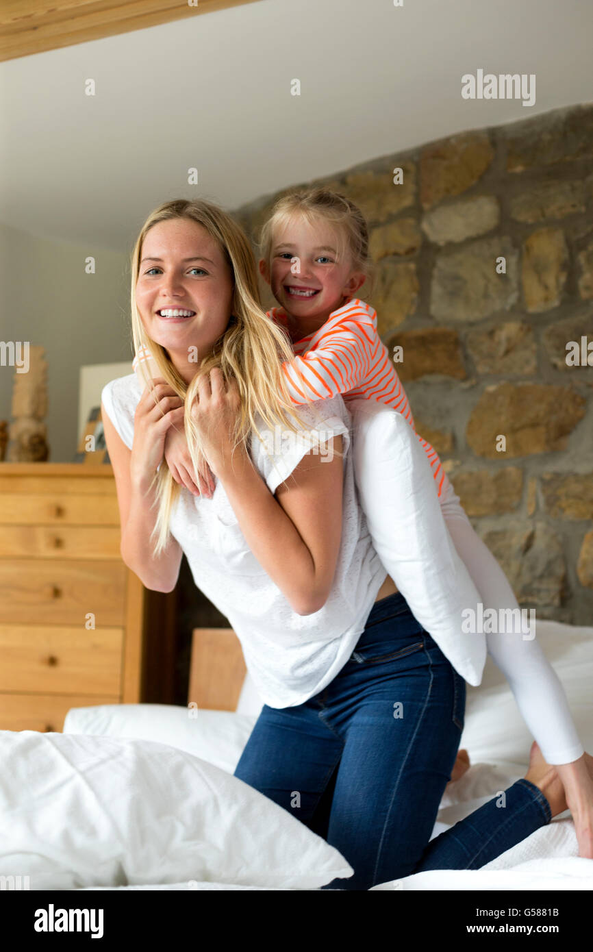 Mère et fille jouer sur un lit à la maison, souriant à l'appareil photo Banque D'Images