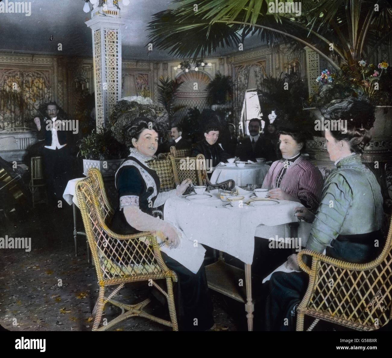 Teatime auf der Titanic, Damen um einen kleinen Tisch sitzen und plaudern, dabei spielt die Bordkapelle. Le voyage inaugural du Titanic Titanic 1912 - catastrophe - l'heure du thé à bord pour les passagers de première classe - Carl Simon, lame de verre colorée à la main - histoire, historique Banque D'Images