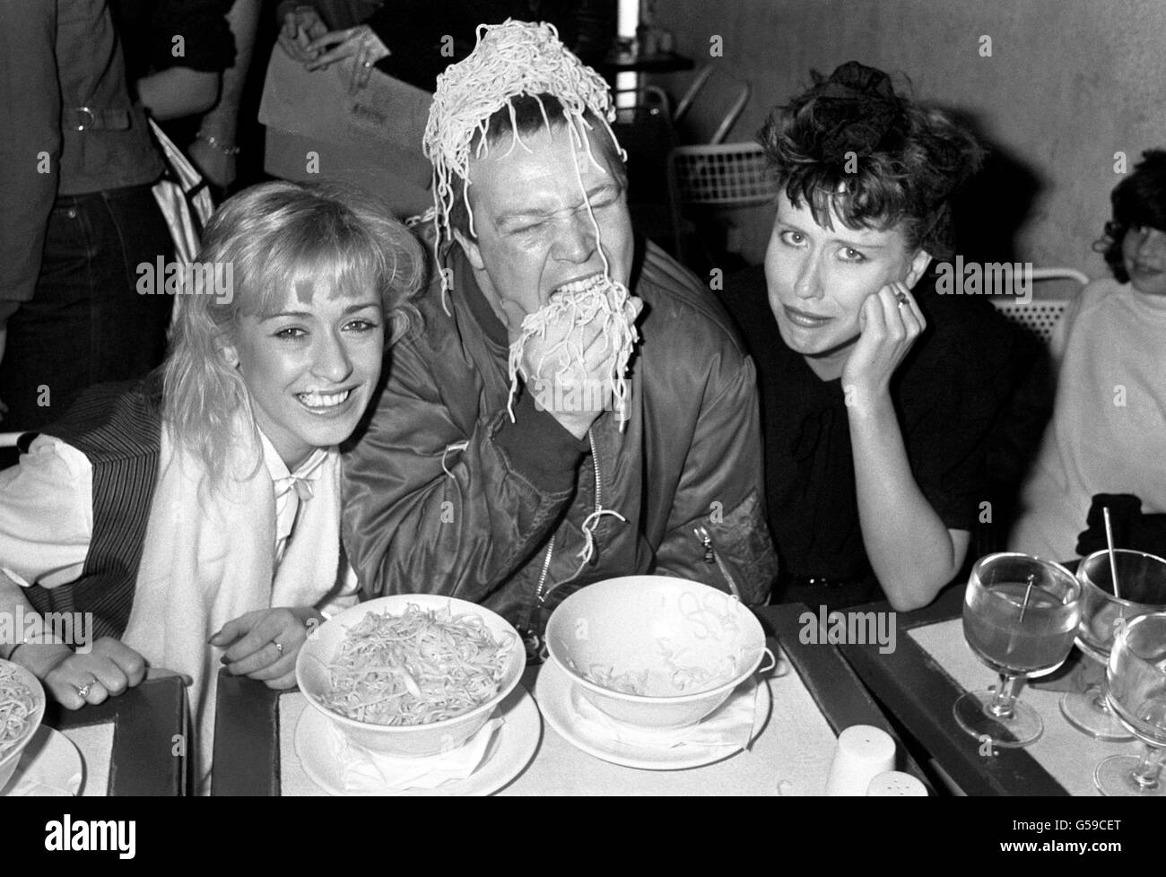 Le chanteur Buster Bloodvaisseau du groupe Bad Manners se livre à des spaghetti au Fatso's Pasta joint à Londres, où il faisait partie de l'équipe de jugement dans un concours de nourriture à spaghetti.Assis avec Buster sont Tereza Bazar (L) du groupe pop Dollar et chanteur/actrice Hazel O'Connor.(R) Banque D'Images