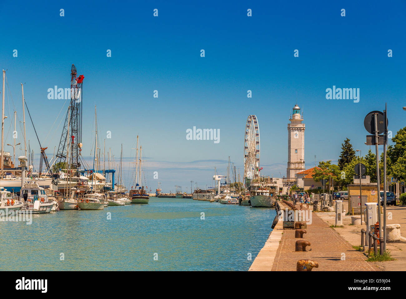 Bateaux amarrés dans le chenal du port de Rimini, Italie avec roue de Ferris et phare en arrière-plan Banque D'Images