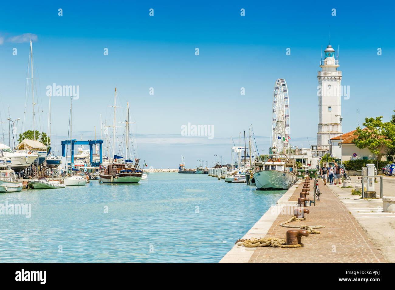 Bateaux amarrés dans le chenal du port de Rimini, Italie avec roue de Ferris et phare en arrière-plan Banque D'Images