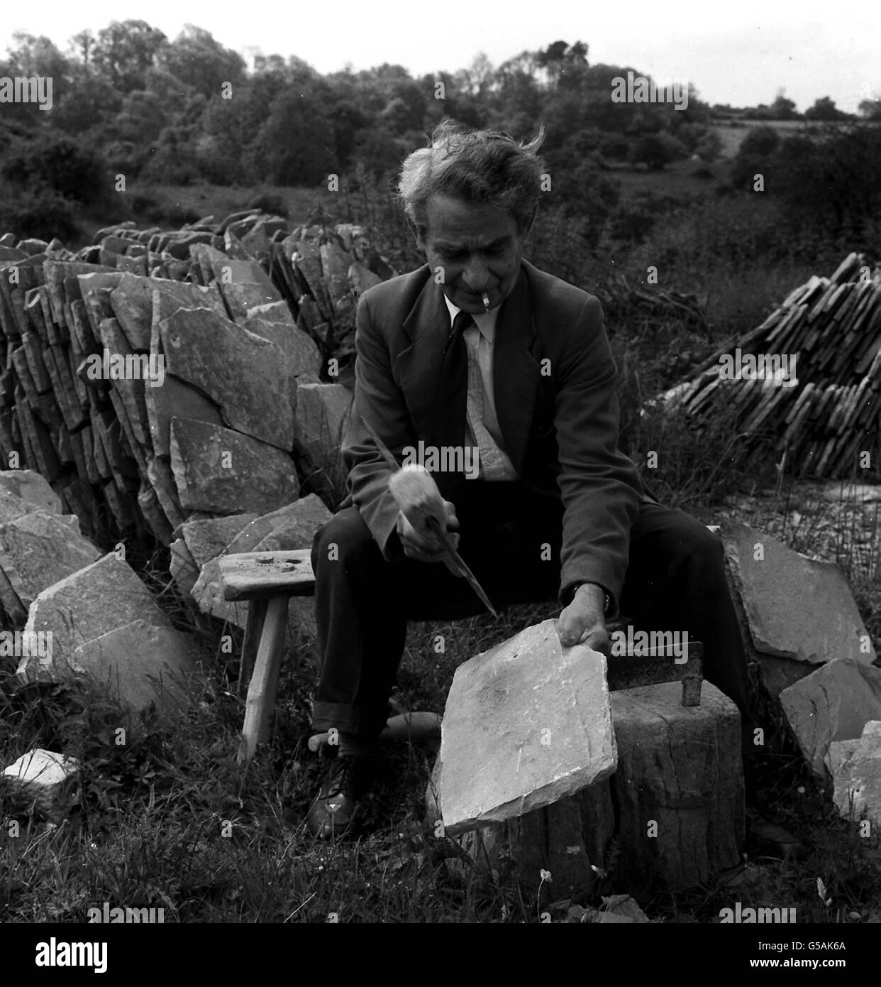 COTSWOLD QUARRYMAN 1964: M. Manoel Da Silva Bandeira au travail dans une carrière de Naunton, Gloucestershire.Il fait le trou de suspension pour un carreau de toit à l'aide d'un pic d'ardoise - une opération délicate.Au tournant du siècle, les Narnton quarrymen pouvaient être numérotés en centaines. Banque D'Images