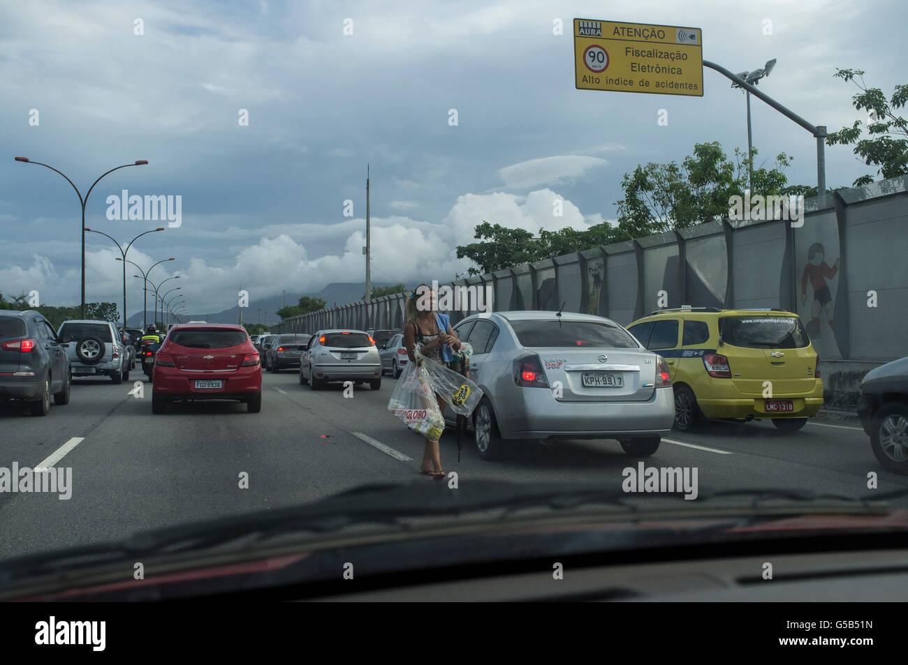 Vendeur de rue fonctionne pendant les heures de pointe de la confiture à l'autoroute Linha Vermelha ( ligne rouge ), principale liaison entre Rio de Janeiro / Antonio Carlos Jobim International Airport et de la ville - en plastique dur opaque division entre l'autoroute et Favela da Mare, zone dominée par le trafic de drogue. Banque D'Images