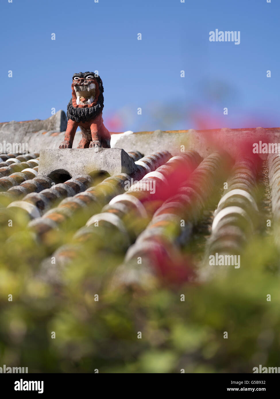 Shisa Okinawa talisman assis sur le toit de tuiles traditionnelles d'une maison avec hibiscus dans l'avant-plan Banque D'Images