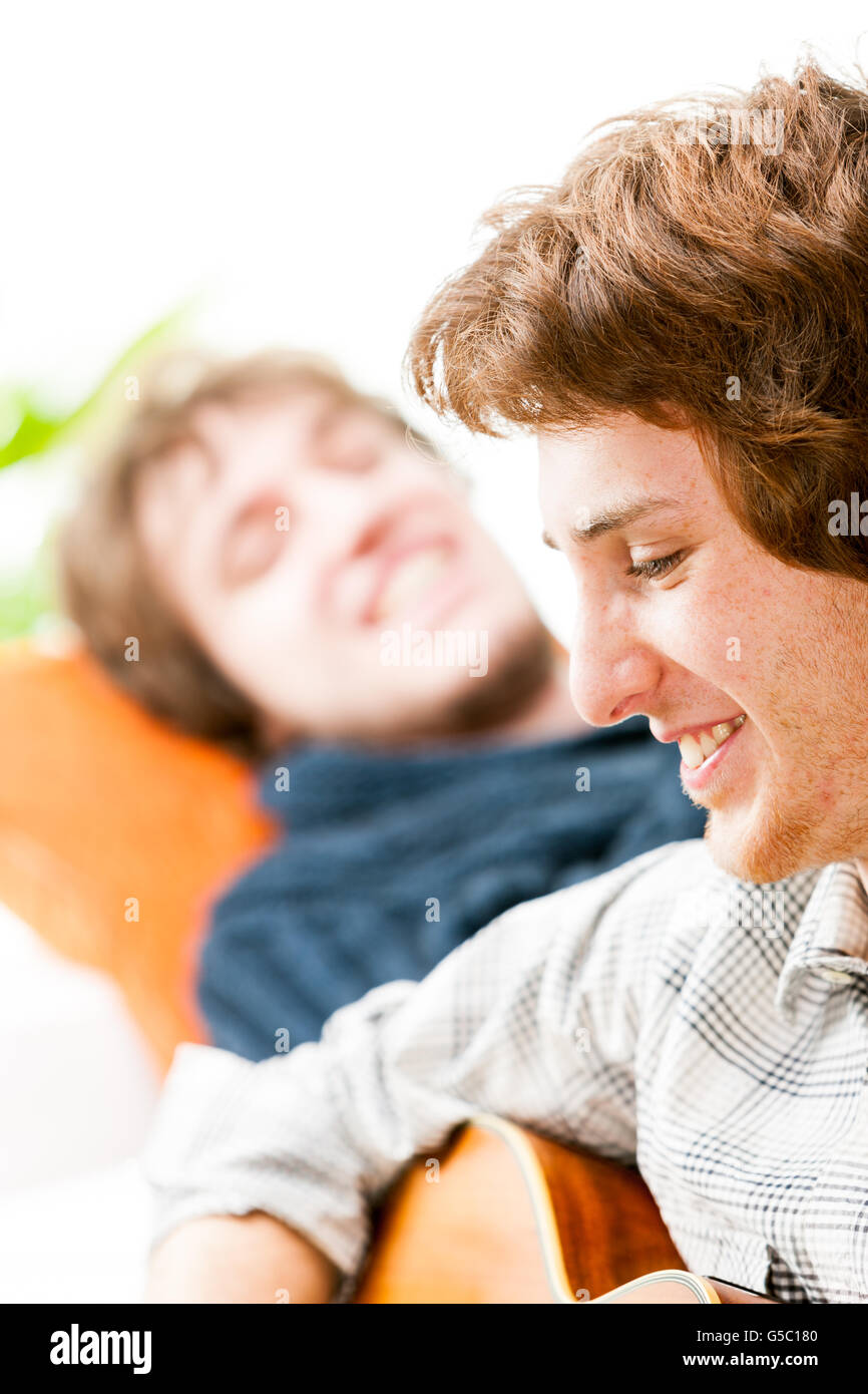 Beau jeune homme qui joue de la guitare pour un ami ou un frère comme ils se détendre ensemble à la maison, Close up profil face Banque D'Images