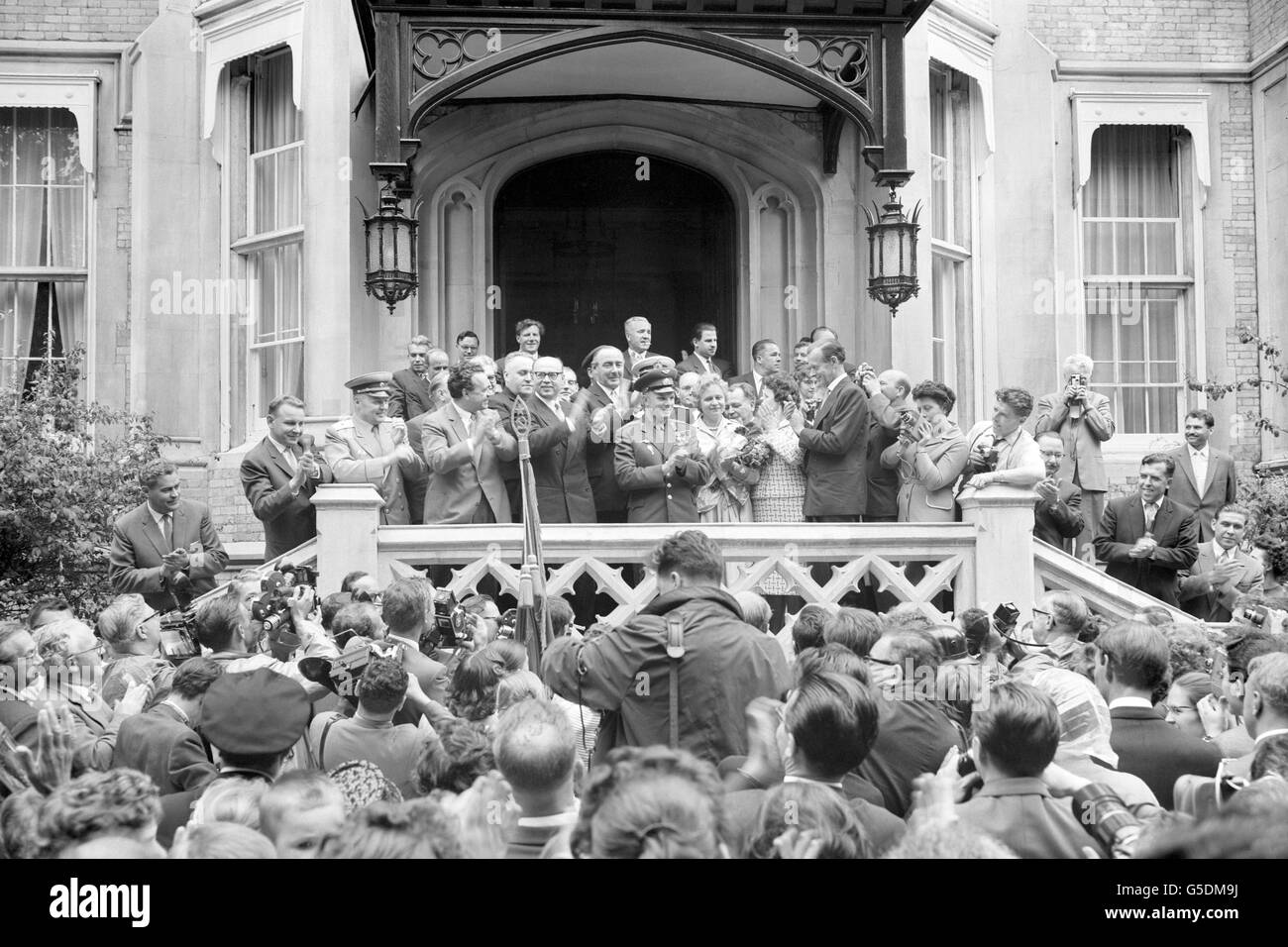 Le cosmonaute russe, le Major Yuri Gagarin, applaudit les applaudissements de l'entrée emballée alors qu'il fut accueilli à son arrivée à l'ambassade soviétique dans les jardins du Palais de Kensington, à Londres. En premier plan, ci-dessous, les photographes travaillent dans une presse de personnes désireuses d'accueillir le premier homme à voyager dans l'espace. Le major Gagarin venait d'être conduit depuis l'aéroport de Londres pour commencer une visite en Grande-Bretagne. Banque D'Images