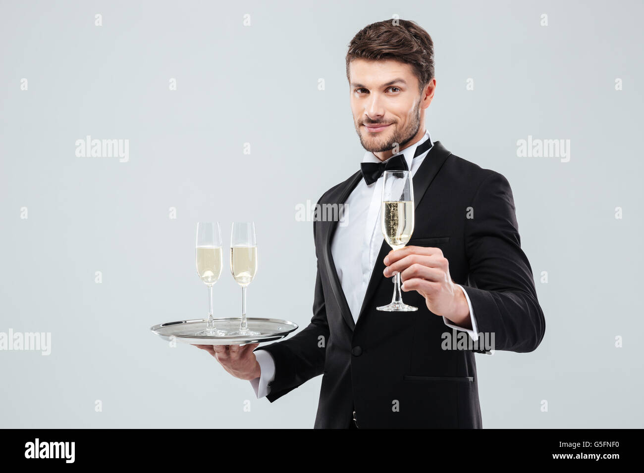 Young waiter in tuxedo holding tray et verre de champagne Banque D'Images