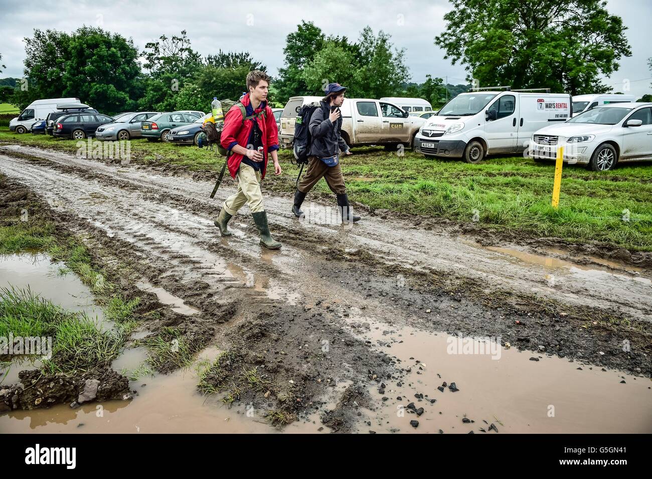Les gens arrivent et parc dans les champs boueux et détrempés à Glastonbury Festival à la ferme digne, Somerset, où de fortes pluies sur une période prolongée a provoqué des inondations isolées et les champs boueux. Banque D'Images